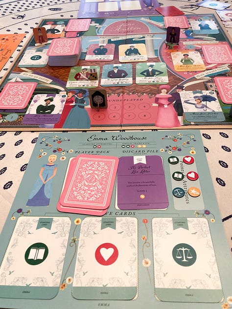 The boxes for "The Jane Austen Game," "The World of Jane Austen" puzzle, "Matchmaking: A Jane Austen Memory Game," and "Jane Austen Playing Cards." Image 2: The game board during a round of play for "The Jane Austen Game." The many pieces are assembled on the board. Image 3: The Emma Woodhouse character board and character cards during a round of play of "The Jane Austen Game." Image 4: Cards from both "Matchmaking: A Jane Austen Memory Game" and "Jane Austen Playing Cards" are spread out on a table next to "The Jane Austen Game" and "The World of Jane Austen" puzzle. Image 5: A close up of the cards from "Matchmaking: A Jane Austen Memory Game" 