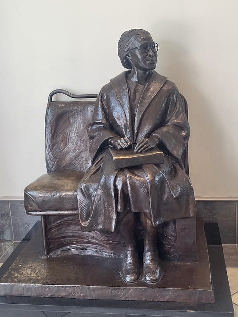 Bronze of Rosa Parks, historic marker by MLK's Dexter Avenue Baptist Church, names of justice nonprofits etched into a black wall, tomb-like structures listing those killed by lynching, shown laying like a coffin and hanging above