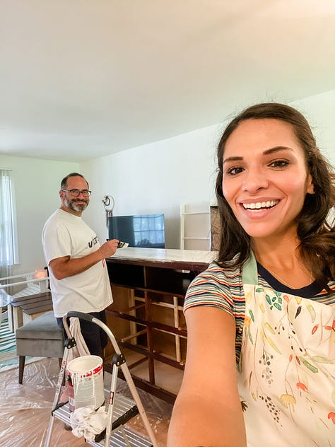 Photo of a paved walking trail surrounded by lush vegetation and a deer on one side, a round embroidery hoop with an image of a pineapple, a woman smiling and presenting the piles of fresh pasta she made from scratch, a selfie photo of woman and her dad painting a piece of furniture, a photo of a woman and her mom sitting on the floor painting a piece of furniture, a selfie photo of a woman and her parents sitting down at the dinner table to eat barbecue food, a photo of a woman and her dog looking out the window, a photo of a LOVE sign in a grassy, woody green forest, a selfie photo of a woman with her parents and dog behind her walking in the opposite direction.