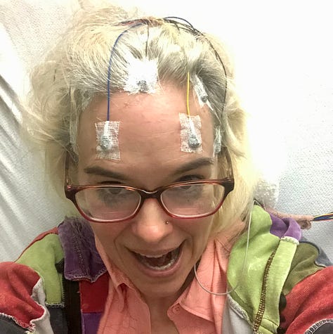 The smart butt author purring at you from over the tops of her glasses with electrodes glued to her scalp, a bird's eye view of the wire-crown, and the heart monitor patches, all over the Hoodie of Many Hues and the obnoxious coral tank top, with the (snigger-snort) luxurious blonde mane corralled in braids.