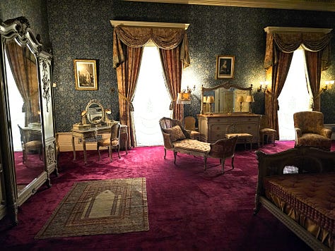 An ornate bedroom with red carpet and gold curtains, and a bathroom with original fixtures.