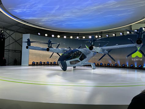 The Supernal S-A2, a sleek aircraft on a round stage surrounded by lights. One photo shows a green-lit interior with four passenger seats.