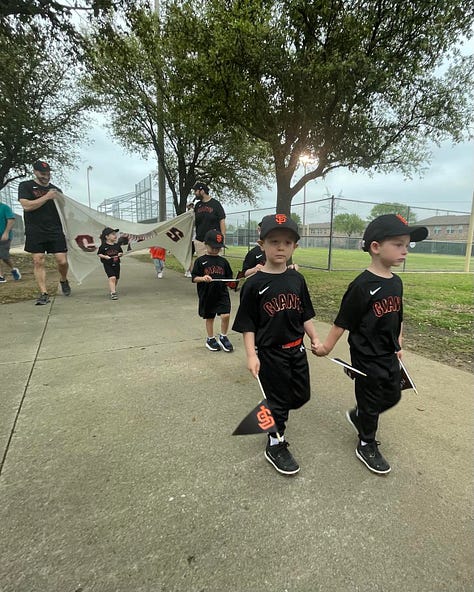 Little boys in baseball uniforms carrying banners bearing their names