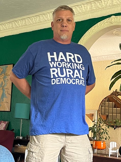 Shy in HARD WORKING RURAL DEMOCRAT tee; in PROTECT TRANS KIDS tee; and in JOHN FETTERMAN'S BODY DOUBLE tee