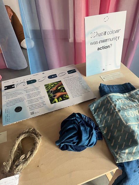 1-3. Exhibition table for 'garden indigos' from Indigo Garden and Fantasy Fibre Mill, showing dyed indigo fabric, processed linen fibre, woad seeds, Japanese indigo pigment, dried Japanese indigo leaves, retted and hackled flax straw and information boards.