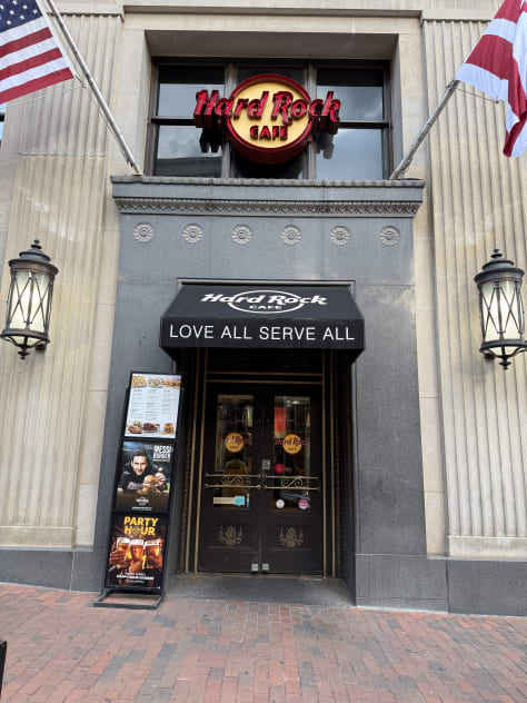 A close-up of the book cover for "18th Abduction" by James Patterson and Maxine Paetro. A person standing at a food cart or street vendor, smiling while holding a hotdog. The front entrance of a Hard Rock Café, with its iconic logo above the doorway. A display of an astronaut suit with the famous quote "That’s one small step for man, one giant leap for mankind" on the wall next to it. A scenic view of a garden or park with a paved pathway leading to a circular pond or fountain.  A close-up of the book "Strange, Dark & Mysterious", a graphic story collection by MrBallen, known for his strange and spooky storytelling.