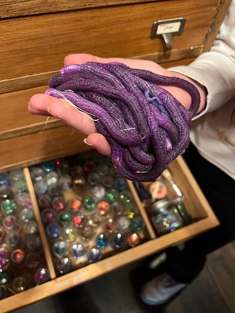 A child looking at a drawer of googly eyes; a drawer full of tiny flocked pine trees and old patches, a hand holding a string of purple vintage sequins.