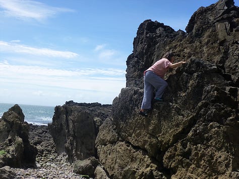 Caucasian woman in pink t-shirt climbing up rocks by the sea
