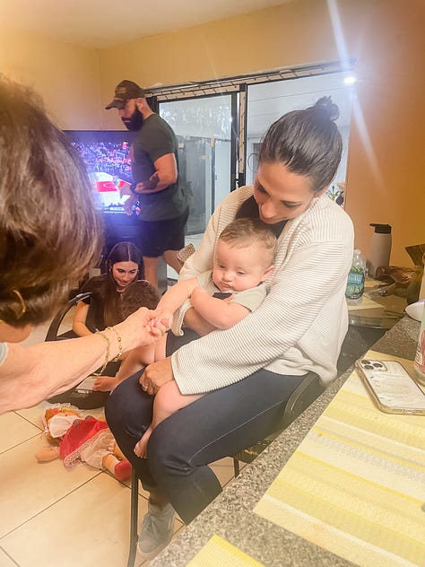 Photo of woman carrying baby boy in her lap with her grandma holding baby's hand; toddler playing with her baby brother on a bed; toddler playing with a bunny rabbit who peeks out from underneath a bed; Two women standing posing at a graduation party in front of a table with a cake, balloons and gifts; a 2-3 foot sized pan of rice with chicken and vegetables; view from a driver's side window of a horse and carriage on the side of a tree-lined neighborhood street; a water bottle with stickers and placeholders for stickers of U.S. National Parks; a photo of a desk with journal, photos, a camera, laptop and other items strewn about; a photo of a cloudy sky where the sky looks like bunches of cotton balls, with the tops of palm trees and city buildings in the latter half.