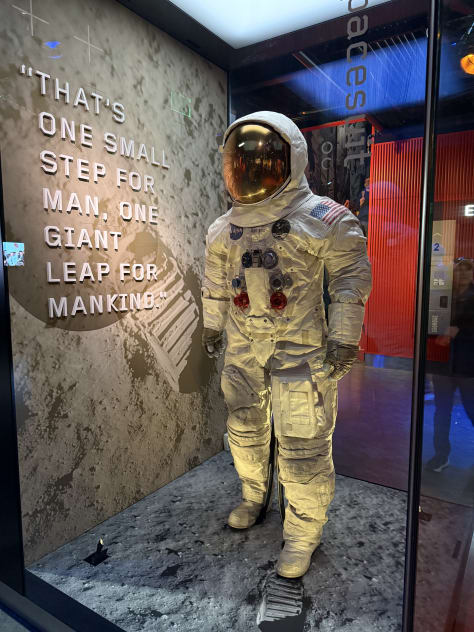 A close-up of the book cover for "18th Abduction" by James Patterson and Maxine Paetro. A person standing at a food cart or street vendor, smiling while holding a hotdog. The front entrance of a Hard Rock Café, with its iconic logo above the doorway. A display of an astronaut suit with the famous quote "That’s one small step for man, one giant leap for mankind" on the wall next to it. A scenic view of a garden or park with a paved pathway leading to a circular pond or fountain.  A close-up of the book "Strange, Dark & Mysterious", a graphic story collection by MrBallen, known for his strange and spooky storytelling.