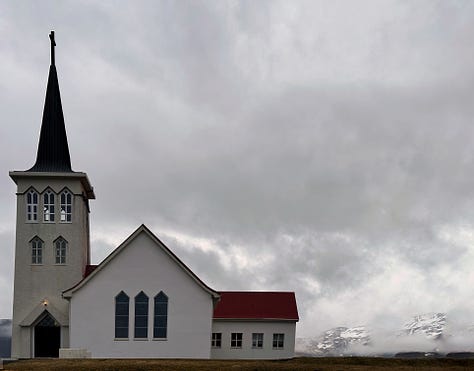 Three images from our time in Grundarfjörður.  1st is our kitchen for the night with light wood cabinets, a small sink, two burners on the countertop and a tiny black refrigerator. 2nd and 3rd views from our walk around town, the mountain as seen from a street looking across the water and small white church with a red roof and tall steeple also painted red.