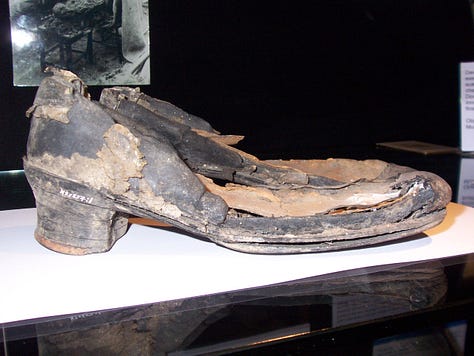 A pair of old shoes, partly decomposed, with patches of leather missing and flaked surface.