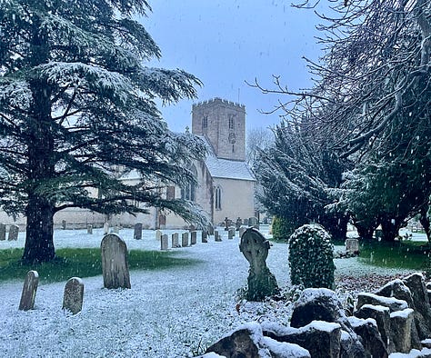 Frosted grasses in a snowy field with a pub in the background; a churchyard with snow on the ground; snow-covered grasses and trees