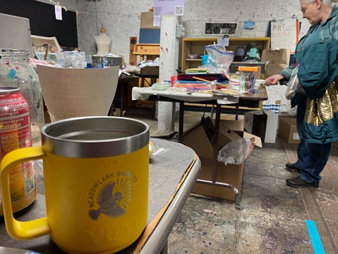 Swappers in a basement space that has filled up with tables and craft materials, clear jars with votes on having the swap again, and a Meadowlark Guide Co coffee mug from a friend who helped arrange materials.