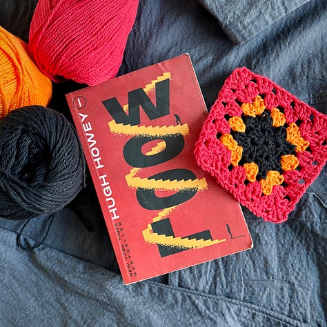 A series of books - Wool by Hugh Howey, The Emporium by Olga Tokarczuk, The Coin by Yasmin Zaher, The Rivals by Jane Pek, Homebody by Theo Parrish, Natural Magic by Renee Bergland, and Eddie Winston is Looking for Love by Marianne Cronin - are displayed with crocheted granny squares next to them that match the colors of the books' covers.