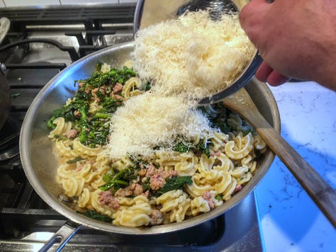 A three-photo gallery of the finishing process 1: The cooked pasta, sausage, and rapini in the skillet 2: A ladle of pasta water being added to the skillet 3: The grated cheese being added to the skillet