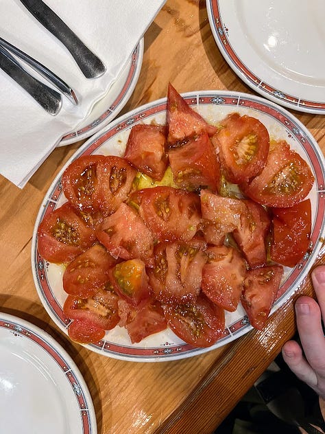 A Bar Nestor employee pouring cider into a glass, overhead shot of a tomato salad, over head shot of a cooked, sliced steak