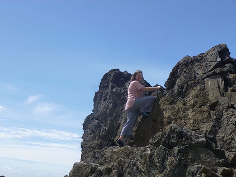 Caucasian woman in pink t-shirt climbing up rocks by the sea