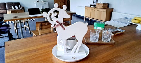 Six photos of stag decorations. 1. cushion with stag head; 2.  2 small black wooden deer ornaments; picture in frame of stag against blue background with message 'Season's Greetings'; white wooden stag figure; two silver stags facing each other with their antlers as candleabra; delicate white ceramic stag tree decoration.