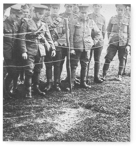 The zeppelin's metal scaffold structure lays in a field, several stories high. Officers inspect the structure and a crowd waits behind a taped cordon.