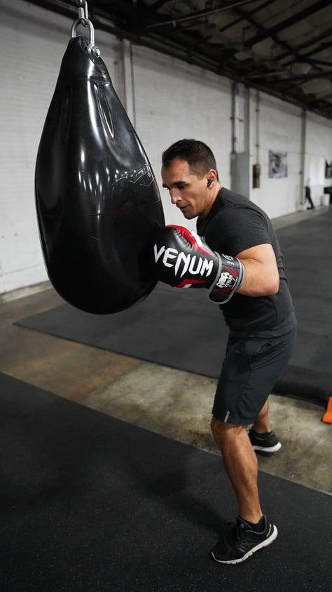 Brian hitting a punching bag at the back of a gym.