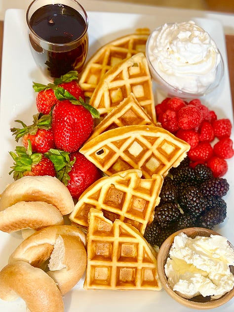 A platter with waffles and strawberries and then blue berries and then complete with bagels, cream and butter