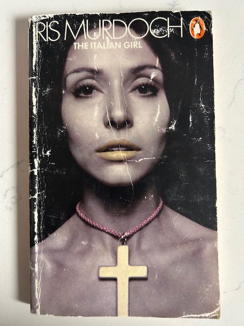 The Italian Girl by Iris Murduch cover has a young woman's face. Around her neck is a necklace with a cross.