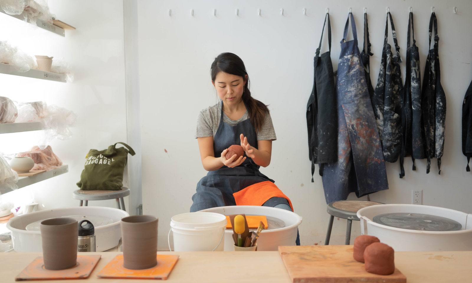 Janice sitting in the center preparing clay for her potters wheel inside a pottery studio.