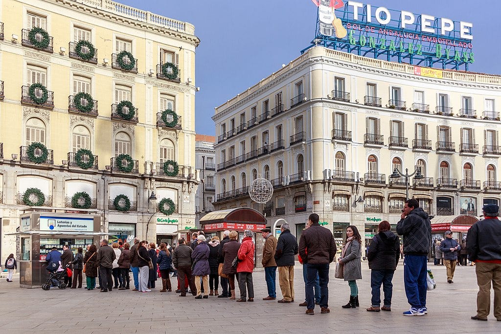 Una fila di persone che attendono di comprare un biglietto della lotteria in uno dei punti vendita ufficiali di Madrid, nella central piazza Puerta del Sol.