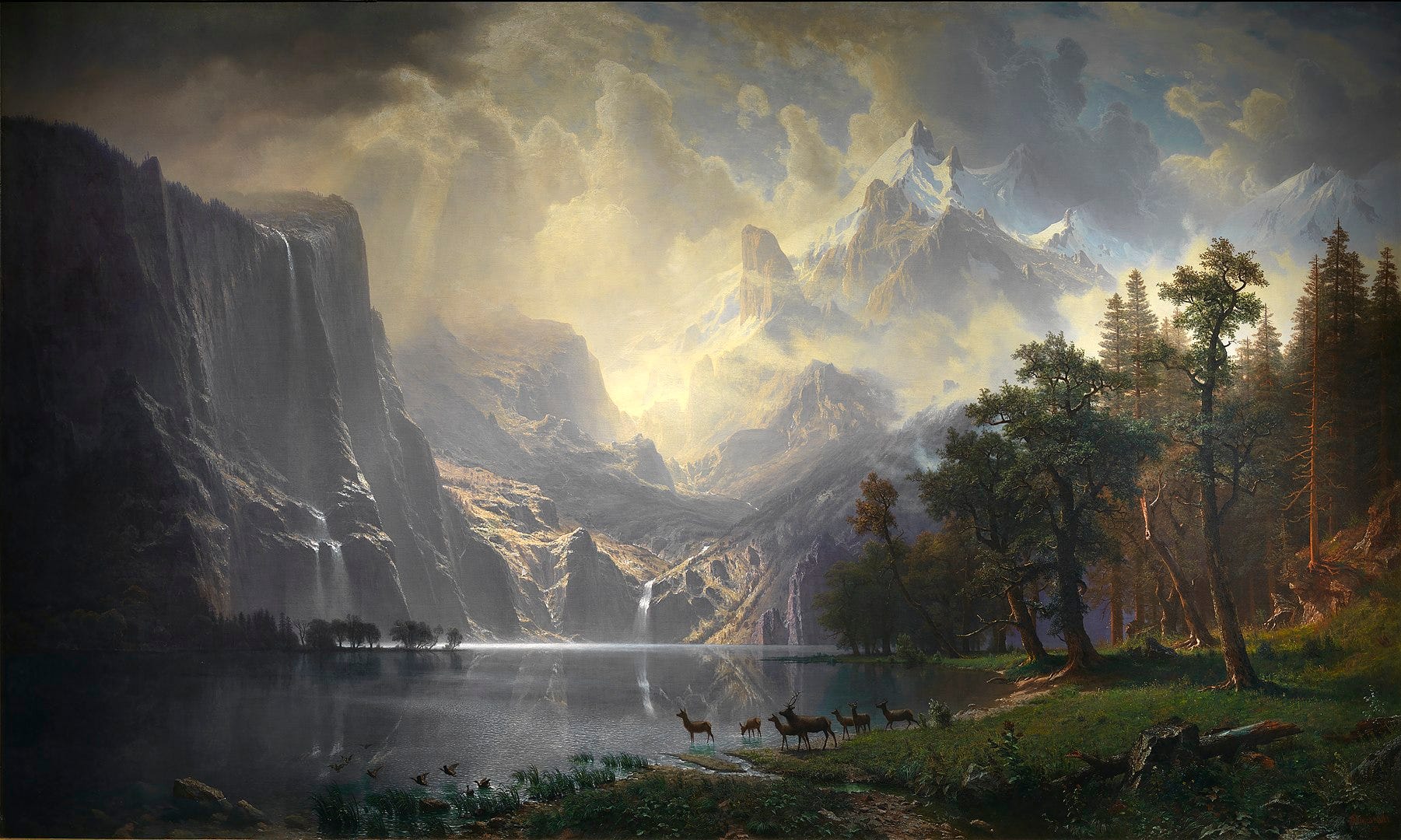 A painting depicts rugged mountains on the left and background that reach out to a bright sky with the Sun's rays peeking through the clouds. The mountains look over a calm lake with a group of deer and waterfowl on its edge and is bordered by trees on the right side of the painting