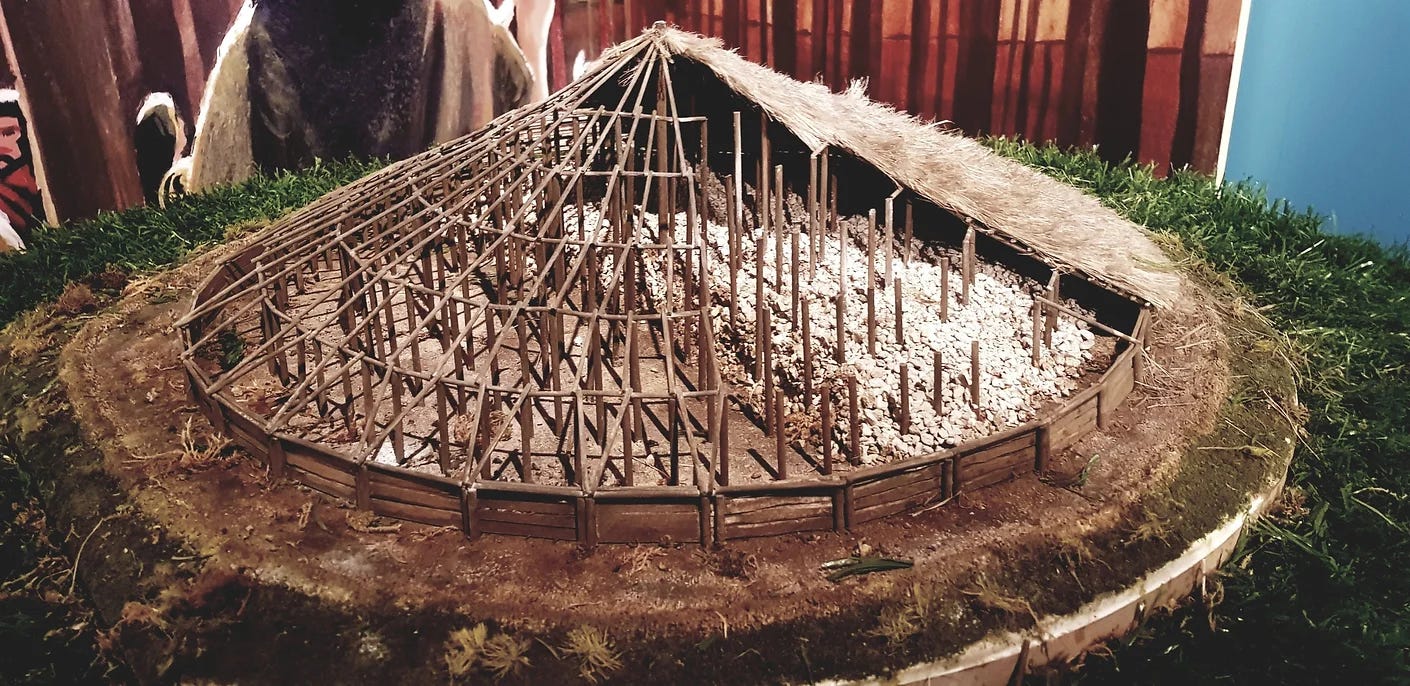 Small model which interprets the site of Mound 2 at Emain Macha, showing a circular structure of raised wooden posts, partly thatched, with a layer of white stones which imitate part of the decommissioning process.