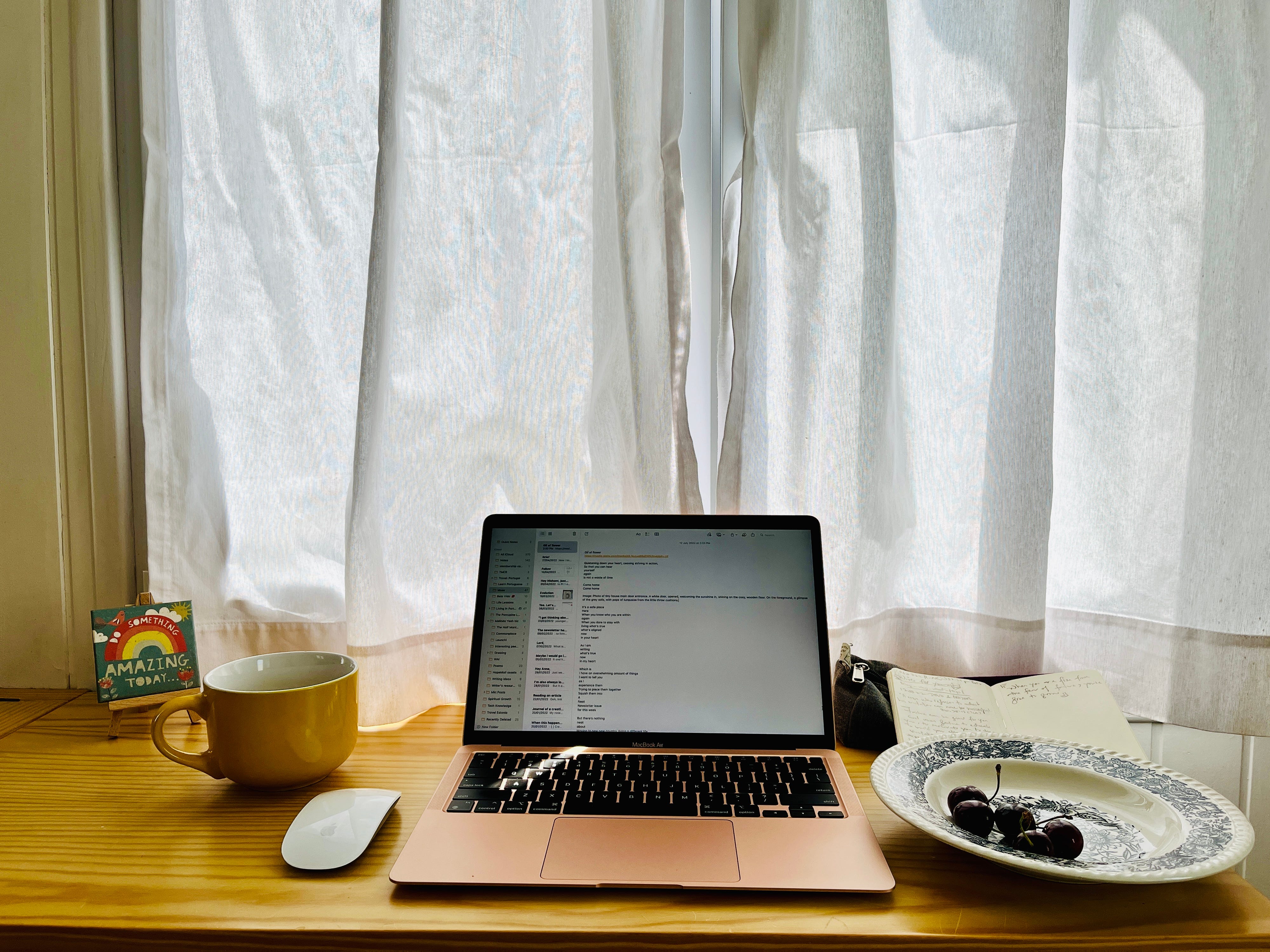 Image: view of where the writer is writing. The wooden bar-like table, overlooks outside, from two big white windows. The curtains are drawn to shield the writer from the summer heatwave. On the left, a small canvas print with the phrase “Do something amazing today”, and the cheery yellow big drinking mug the writer has grown very fond of. And of course, in the centre, as the centre, her Mac where words swim in and out to the world. 