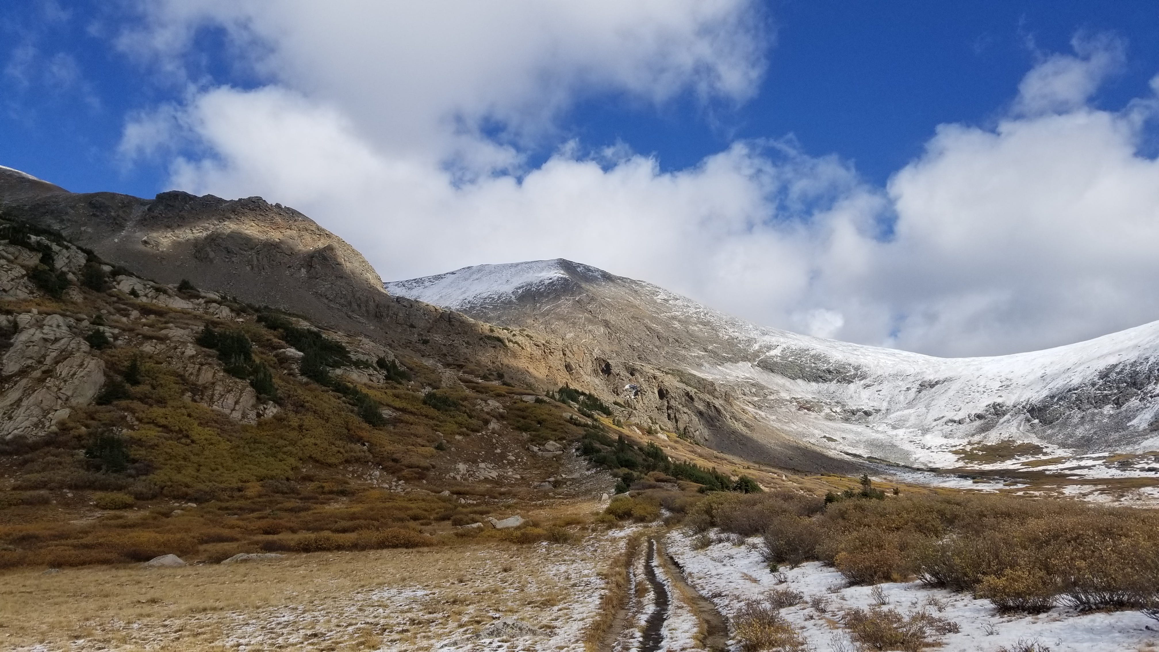 a pathway winds toward a mountaintop, covered in a dusting of fresh, late autumn snow