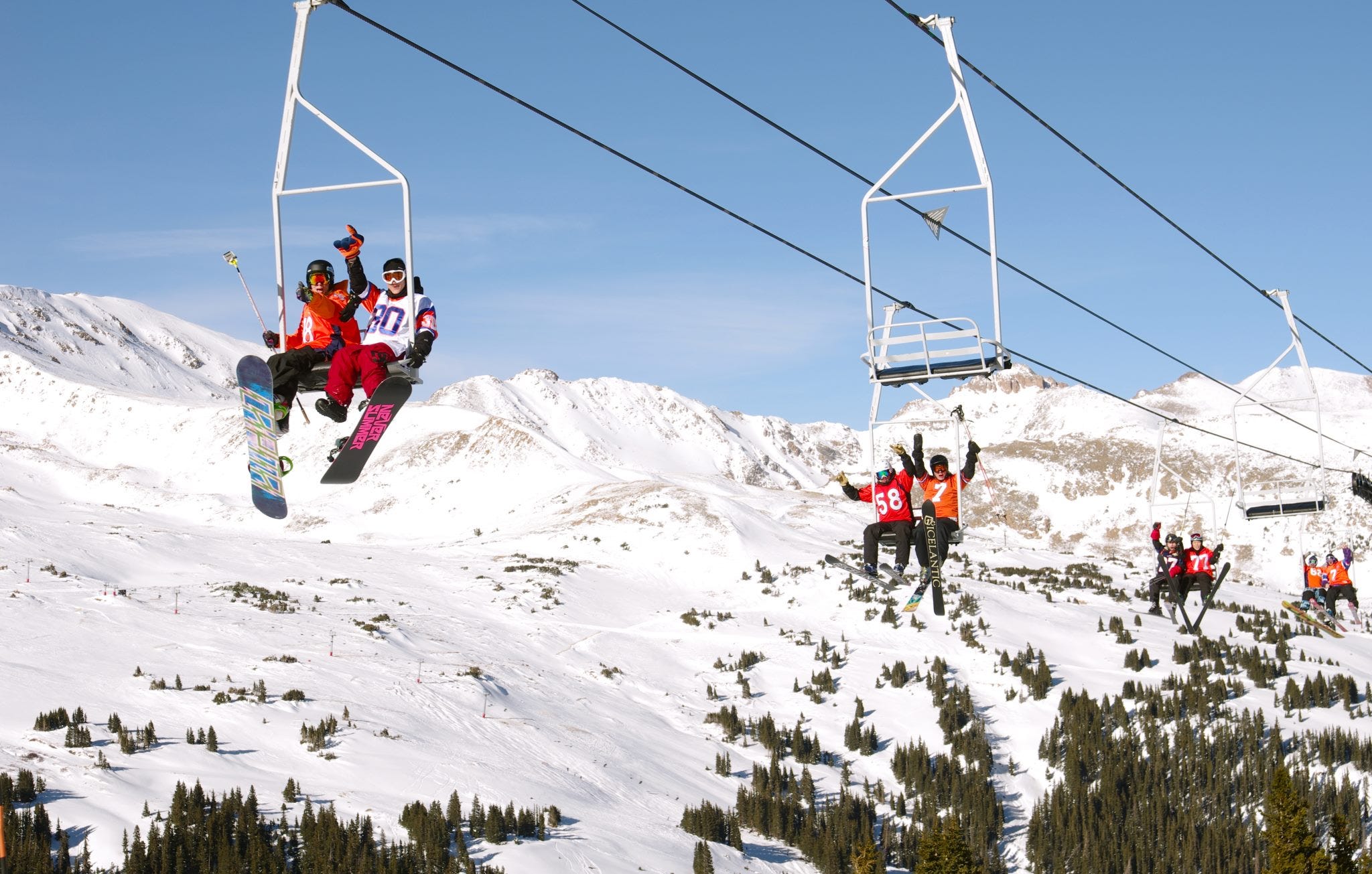 riders zip up Loveland Ski area on Chair 6, with a blue sky and snow-capped peaks in the background