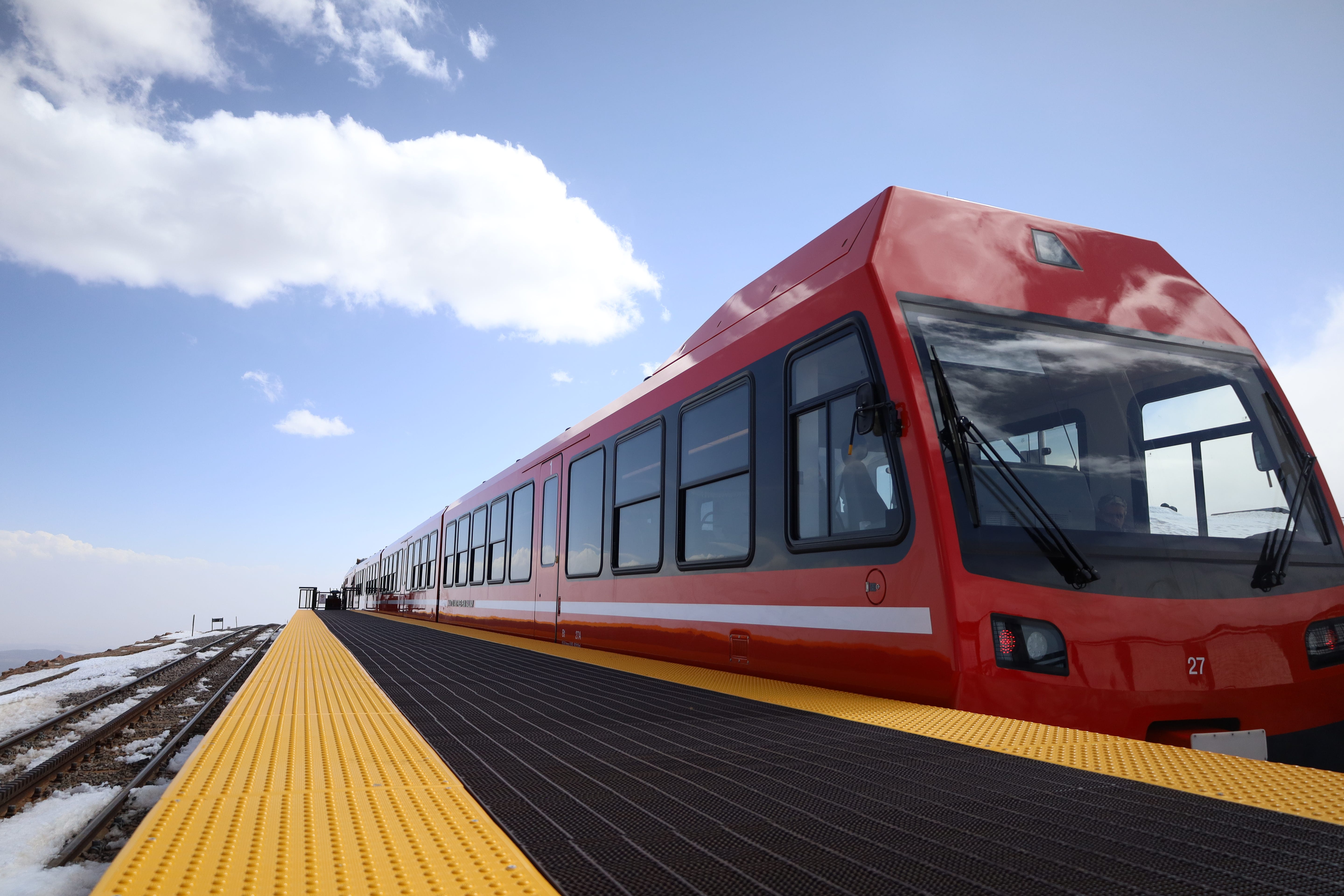A bright red train at the platform, with a vibrant blue sky in the backdrop