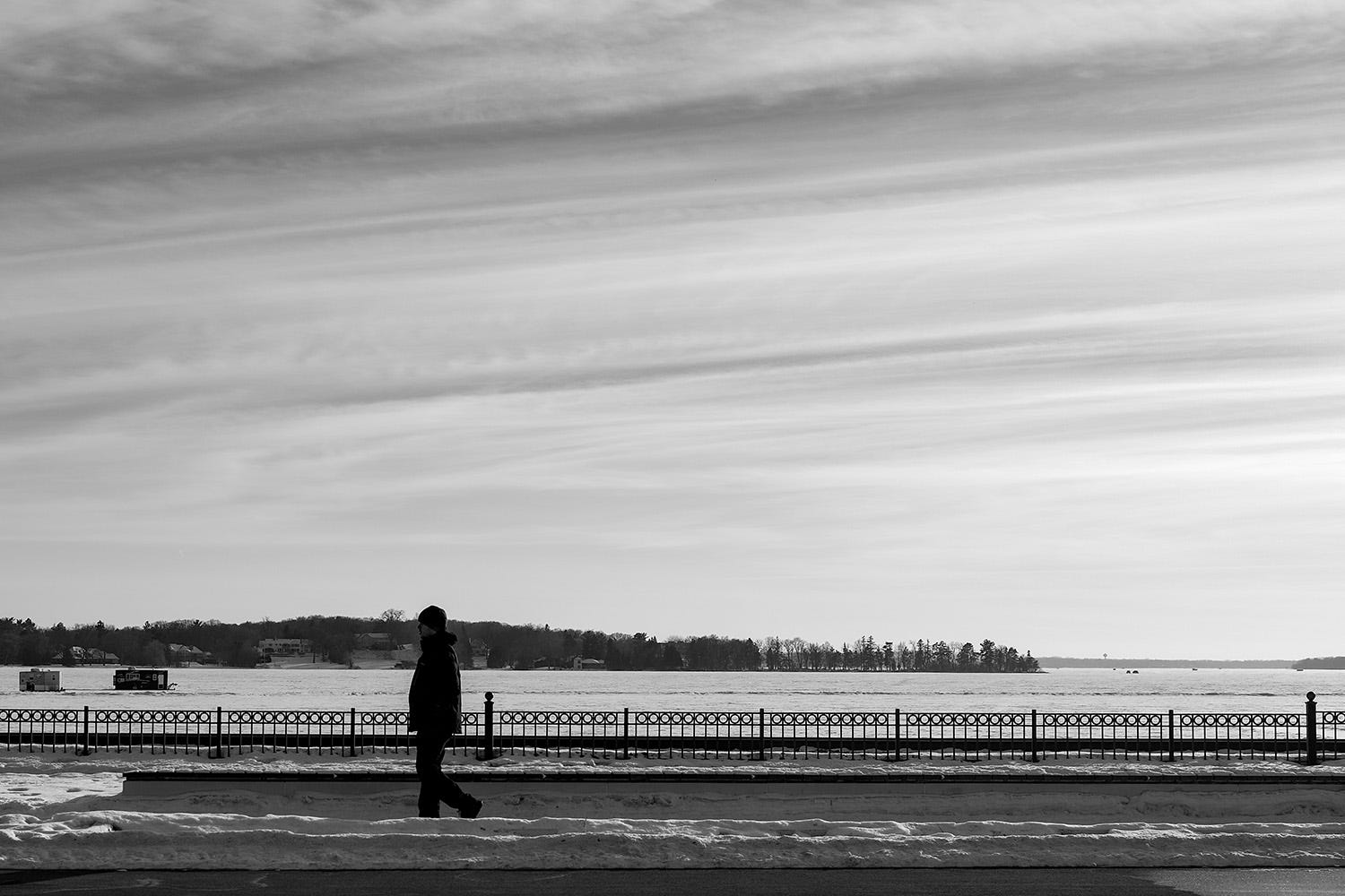 A man walks from right to left in front of the view of the frozen lake. 