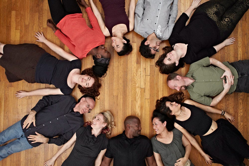 A circle of diverse individuals lying on the ground and looking at one another