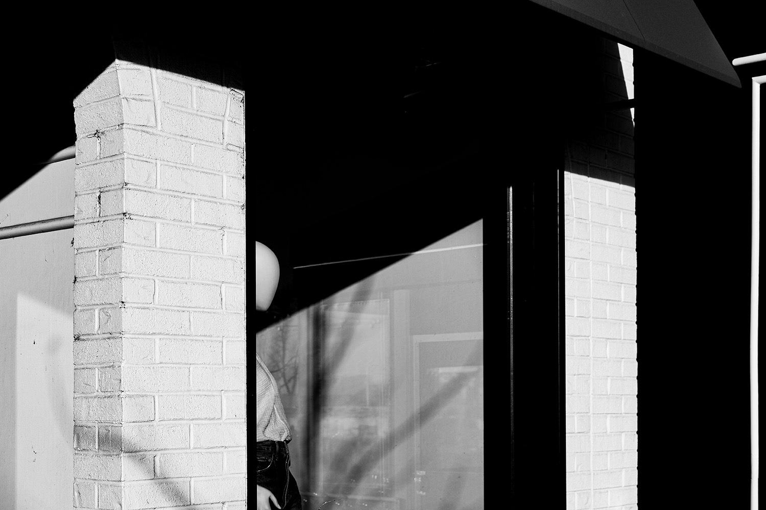 A mannikin is positioned in a shop window. Late afternoon sunset highlights the mannikin amongst the geometric scene full of light and shadows. 