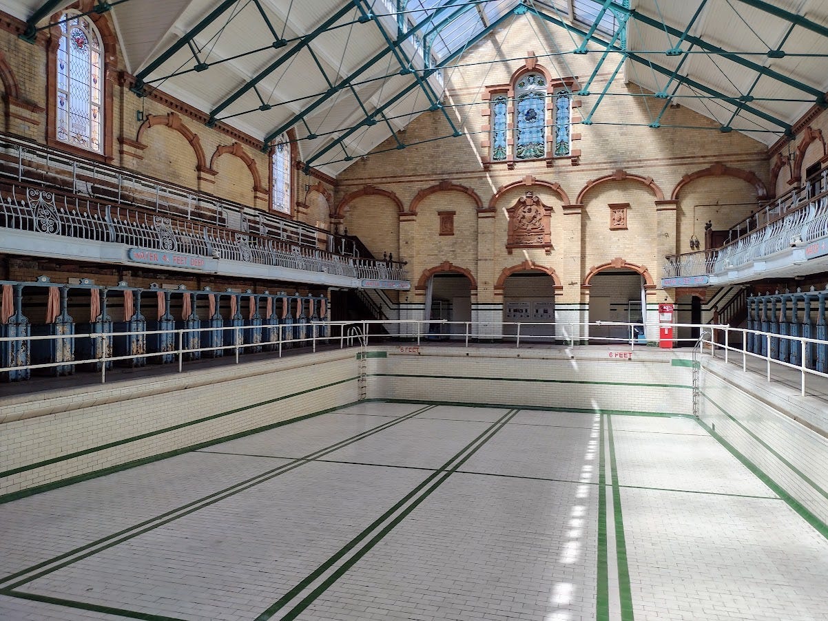 Huge indoor pool with vaulted ceiling, tall mulllioned windows, seating above, booths on either side below