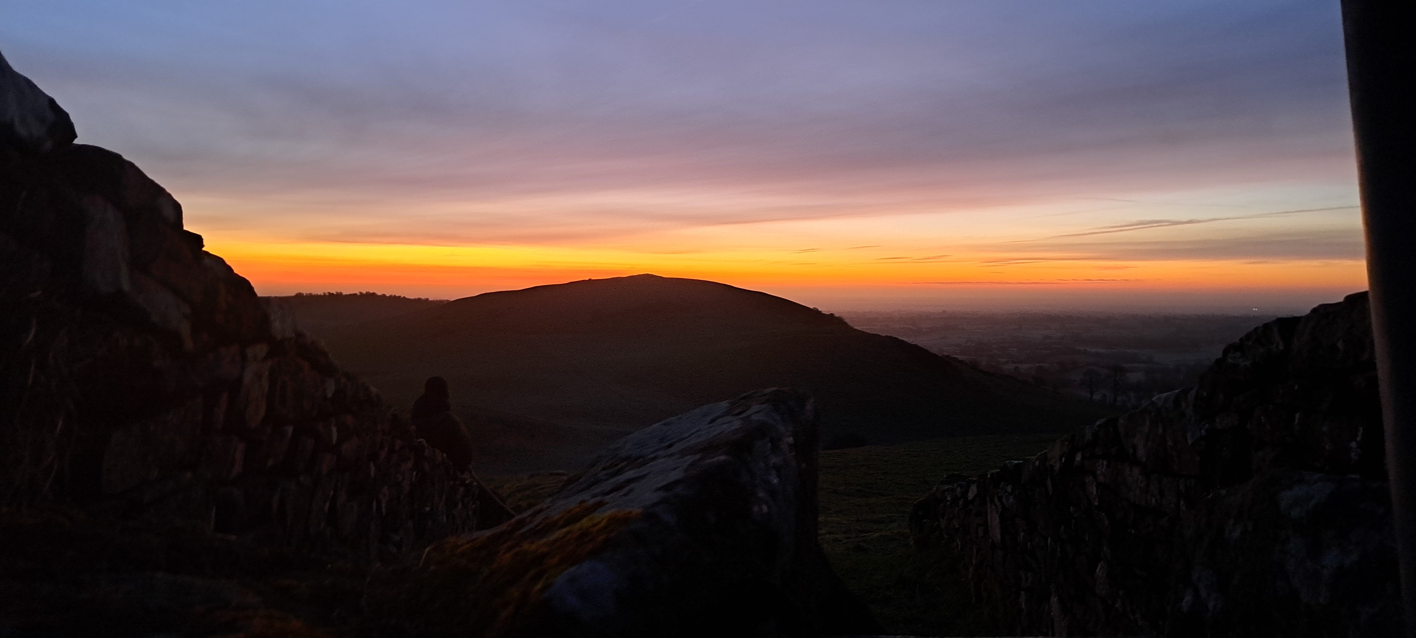 Dawn over the hilld and monuments of Loughcrew, the sky has shades of orange and gold and lilac fading into grey-blue as the sun is about to make an appearance over the hill.