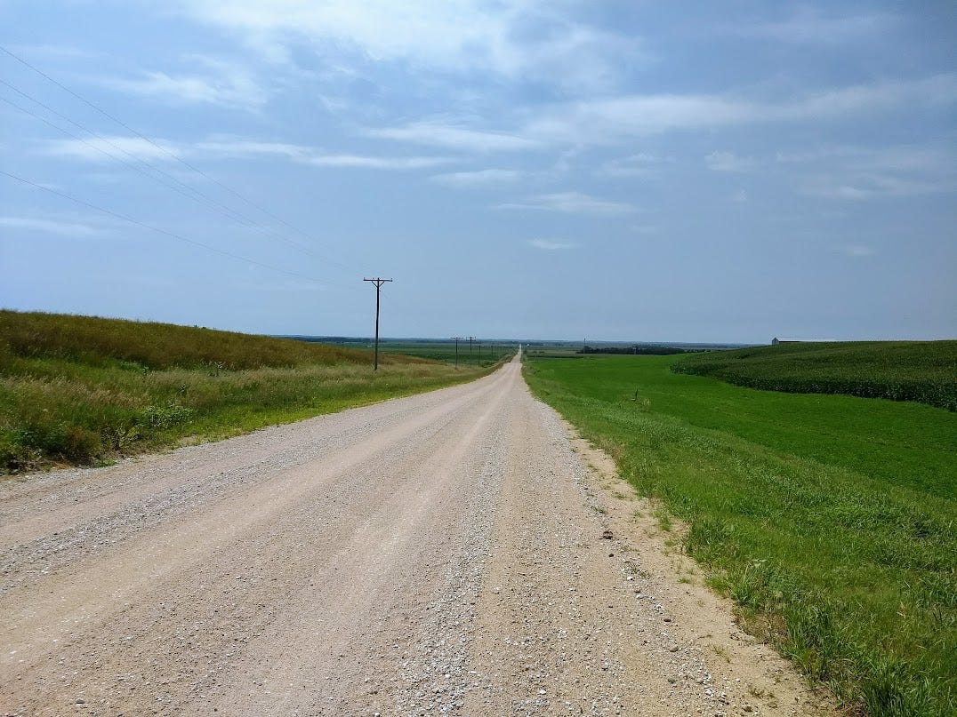 Long dirt road stretching to infinity across grass with utility pole