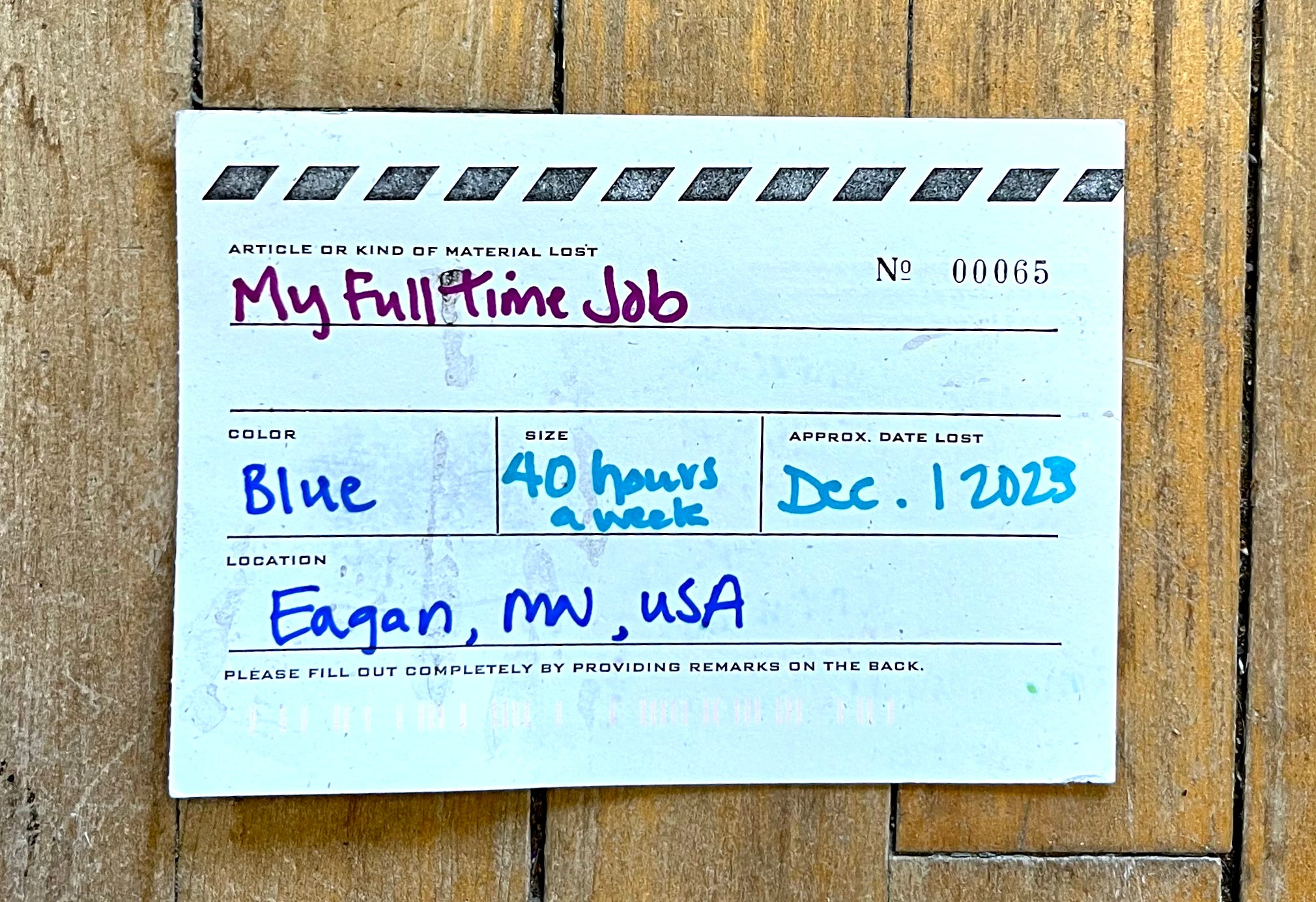 A black and white postcard designed to look like a lost article tag. It is numbered 00065. Under article or kind of material lost it says in handwriting "My full time job". Color: Blue. Size: 40 hours a week. Approx. Date Lost: Dec. 1 2023. Location: Eagan, MN, USA