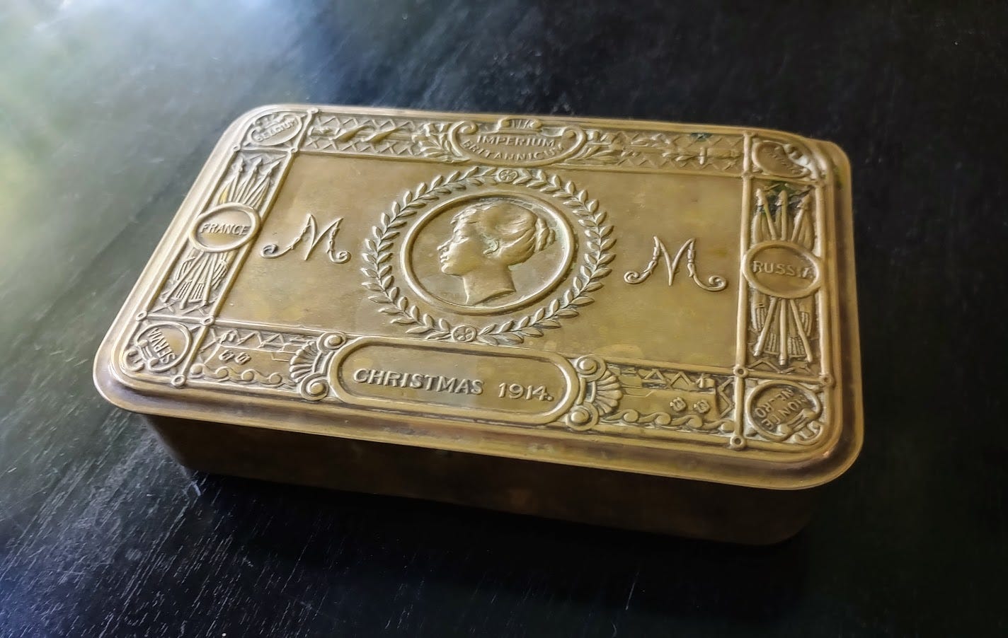 Ornate brass tin with image of woman's head, M monograph, and Christmas 1918 on top. 