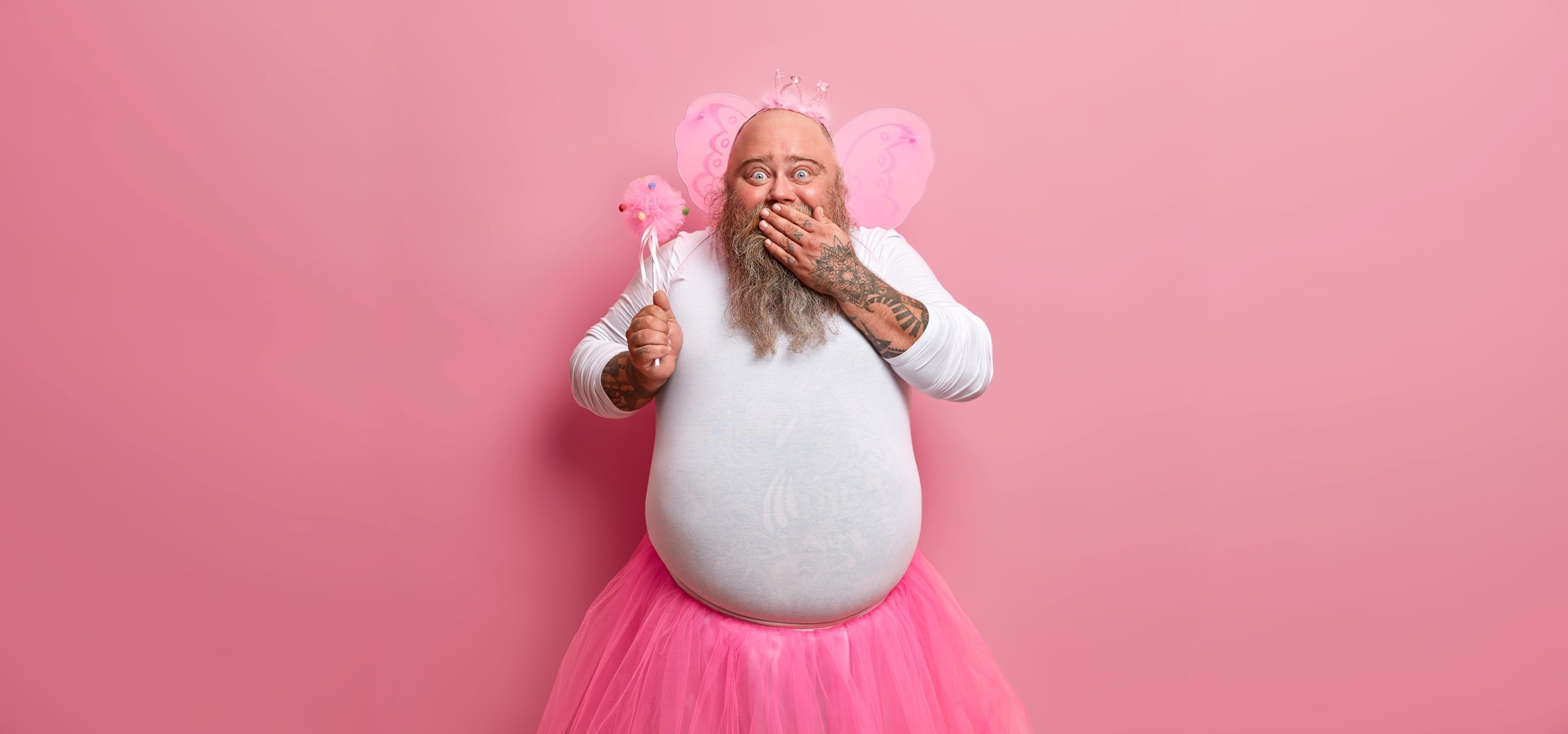 Rotund bearded giggly man wearing a tutu, tiara and tiny wings