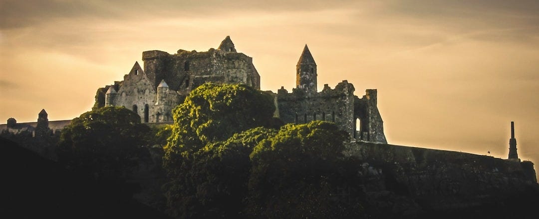 grey stone castle, partly ruined, on top of a hill set against golden sky at sunset