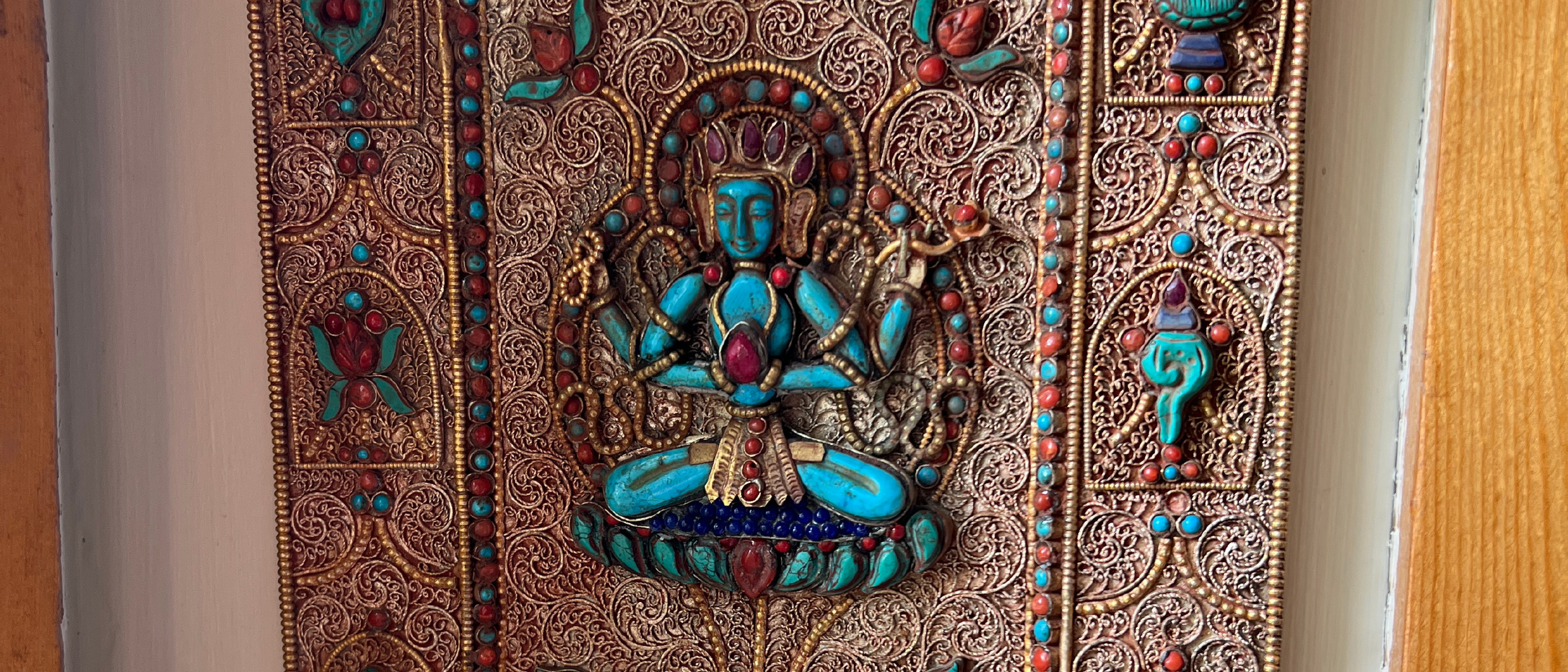 A tightly cropped photograph of a four-armed Chenrezig carved out of turquoise and set in an intricate metal background. 