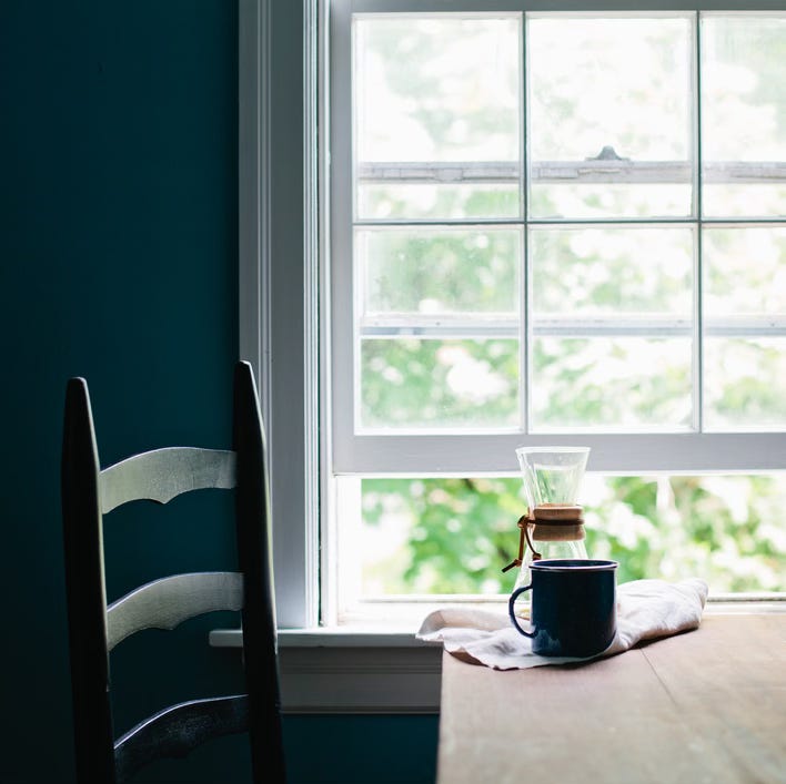 chair sitting next to a table by a window, a carafe of coffee and a mug sitting on the table. sunlight coming in