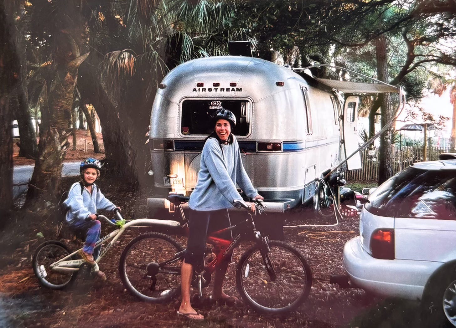 woman and child on tandem bicycle in front of Airstream motorhome at campsite