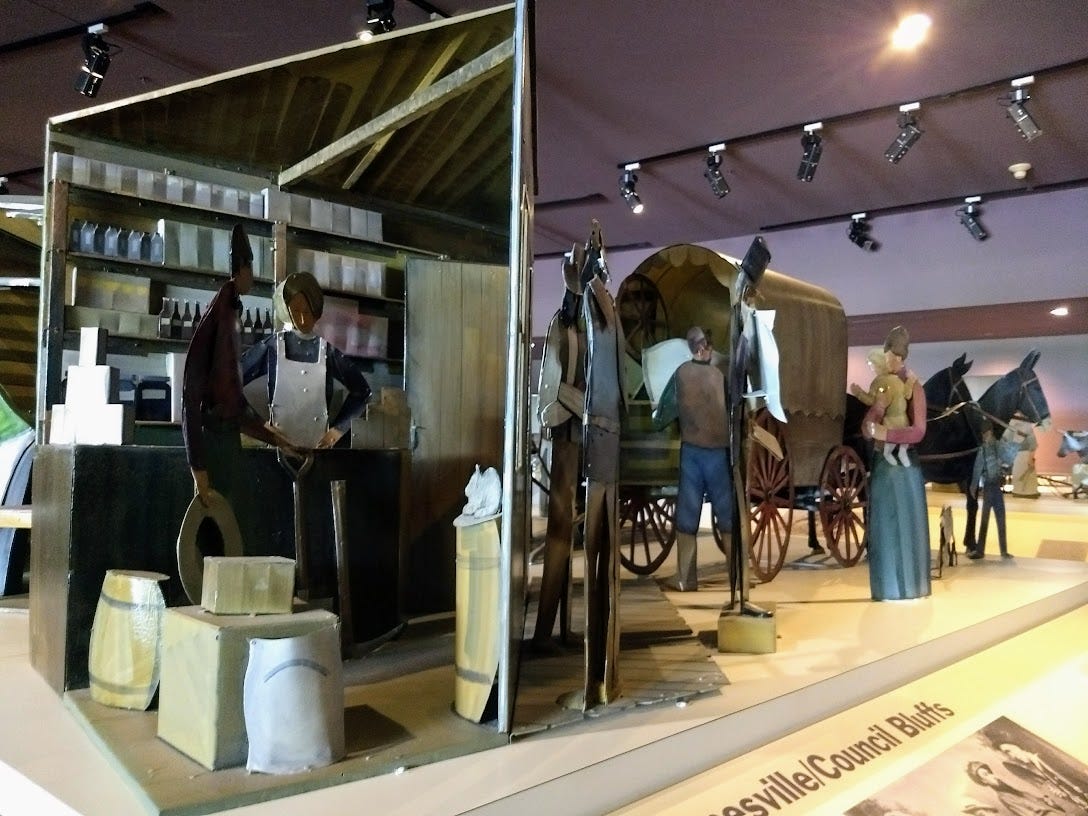 Scene of metal sculptures showing 19th century grocery intierior and people loading wagon