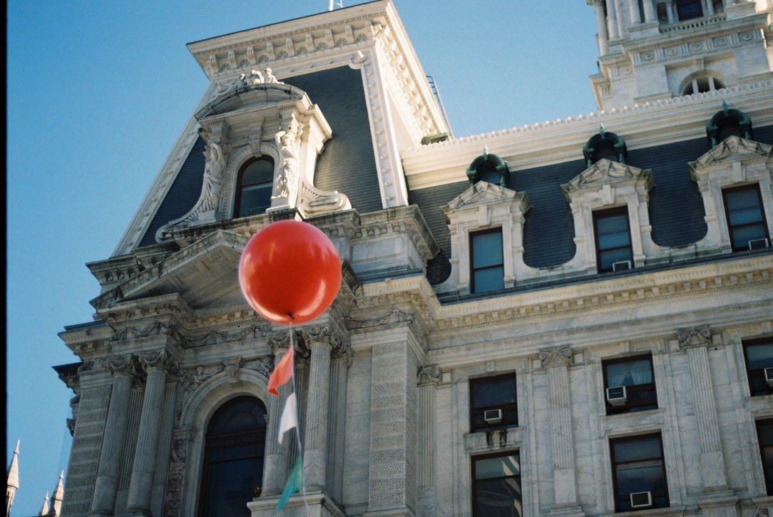 A partial view of Philadelphia's City Hall. A Single red balloon in the foreground is attached to a string with small red, green, and white flags on it.